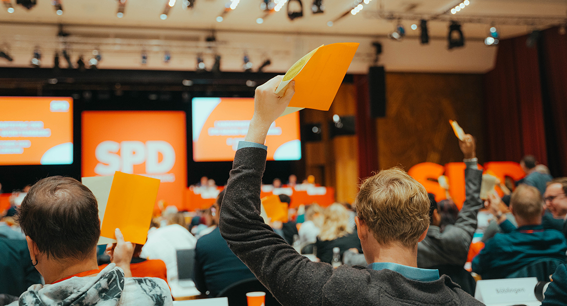 Rückansicht von Delegierten beim Landesparteitag der SPD Baden-Württemberg 2023, die Stimmzettel zu einer Abstimmung hochhalten.