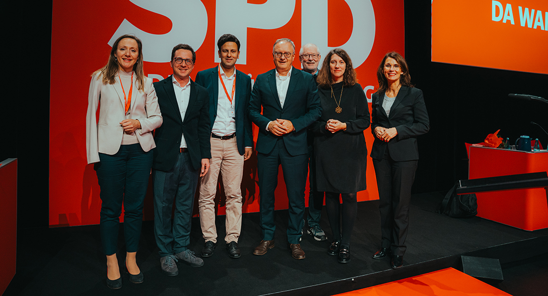 Die Mitglieder des Landesvorstands der SPD Baden-Württemberg auf einem Gruppenfoto vor einer großen Leinwand mit der Aufschrift weiß auf rot: "SPD Baden-Württemberg"